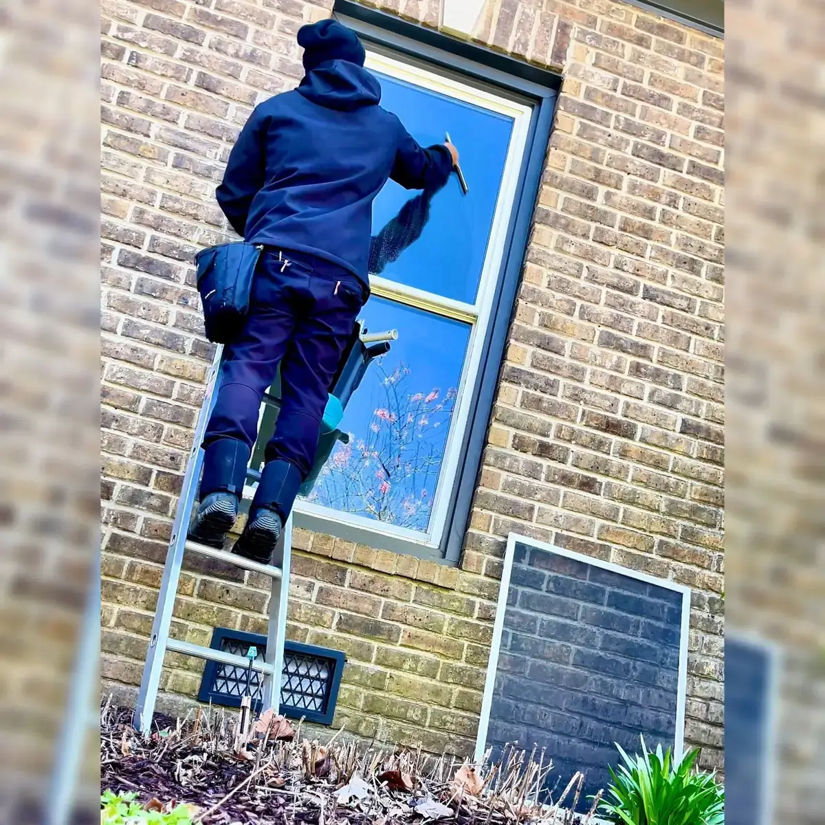 JPS technician cleaning a brick home's window from a ladder